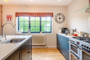 A modern kitchen with a large window, a clock, and a stove. - 3 Bed in Hunstanton (oc-b44904) (Hunstanton)