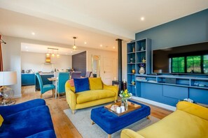 Een moderne woonkamer met een bank, fauteuils en een salontafel. Achtergrond is een keuken met blauwe kasten en een eethoek.