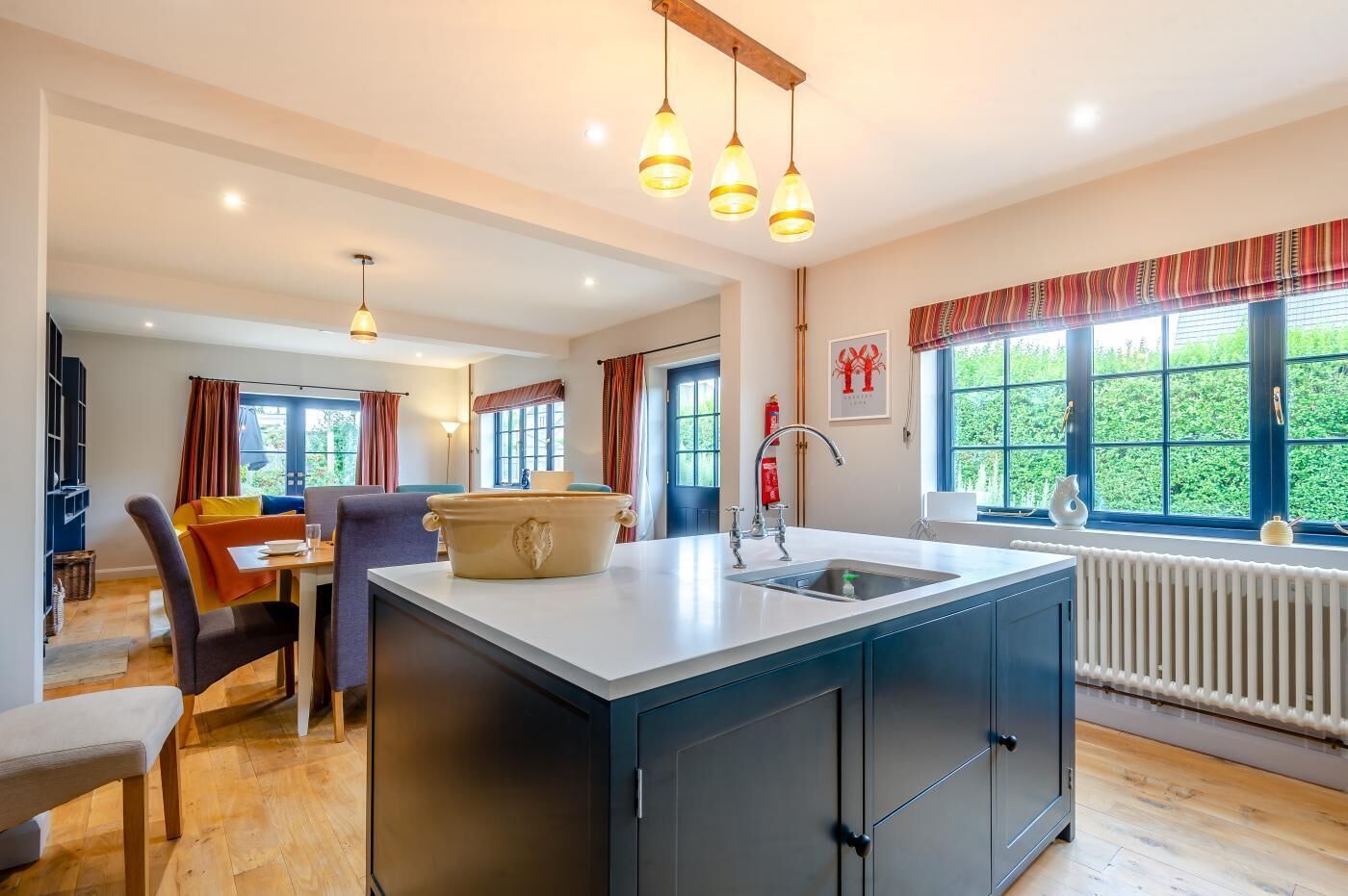 Een moderne keuken met een centraal eiland, hangende lampen en uitzicht op groen.