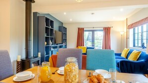Ein gemütliches Wohnzimmer mit Kamin, einem Esstisch mit Frühstück gedeckt und einer komfortablen Sitzecke mit Sofa und Sesseln.