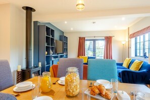 A cozy living room with a fireplace, a dining table set with breakfast, and a comfortable seating area with a sofa and chairs. - 3 Bed in Hunstanton (oc-b44904) (Hunstanton)