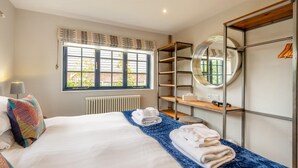 Ein Hotelzimmer mit Bett, Fenster mit Jalousien, Heizkörper, rundem Spiegel und eingebautem Kleiderschrank mit Regalen.
