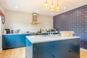 A modern kitchen with a central island, blue cabinetry, a stainless steel range hood, and pendant lighting. - 3 Bed in Hunstanton (oc-b44904) (Hunstanton)