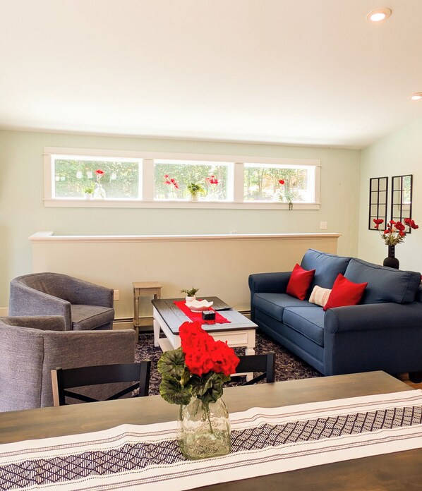 A living room with a blue sofa, a grey armchair, a coffee table, and a vase with red flowers.