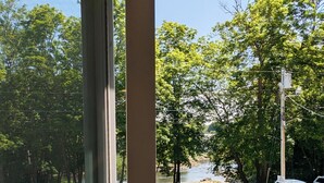 Una terraza de madera con barandilla de metal, sillas rojas y vistas a un río y árboles.