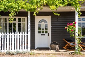 Ein Haus mit weißem Zaun, einer weißen Tür mit Fensterglas und einem Korbwesen auf der Veranda.