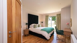 Ein Schlafzimmer mit Bett, Nachttischen, einem Sessel, einem Schreibtisch und einem Fenster mit Vorhängen.