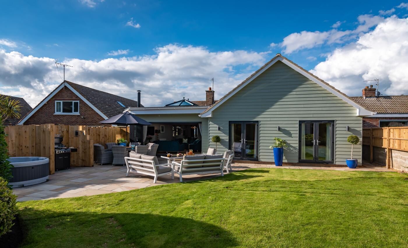 A residential property with a patio, outdoor seating, a hot tub, and a well-maintained lawn.