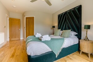 A bedroom with a bed, a wooden floor, a door, a ceiling fan, and a bedside lamp. - 4 Bed in Hunstanton (oc-o44907) (Hunstanton)