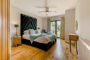 A bedroom with a large bed, a ceiling fan, a view of the outdoors, and a small table. - 4 Bed in Hunstanton (oc-o44907) (Hunstanton)