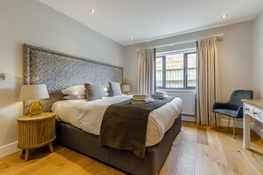 A modern bedroom with a large bed, bedside lamps, a desk, and a window with curtains. - 4 Bed in Old Hunstanton (oc-o44907) (Hunstanton)