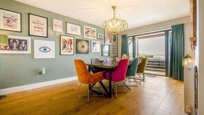 Een eethoek met een houten tafel, kleurrijke stoelen en een kroonluchter.