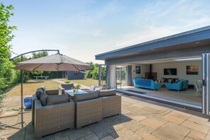 Een moderne buitenruimte met terras, rieten meubilair en een grote parasol.
