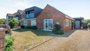 A two-story house with a brick exterior, a front lawn, and a gravel driveway. - 4 Bed in Hunstanton (oc-o44908) (Hunstanton)