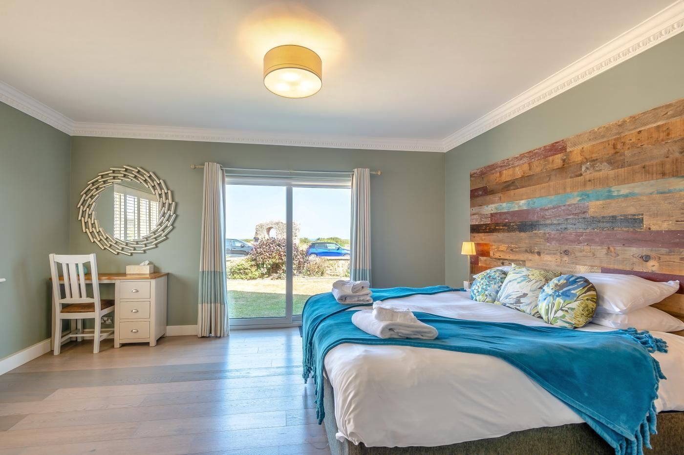 A hotel room with a bed, a desk, a chair, a large mirror, and a view of the outside.