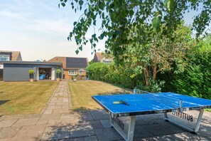 A backyard with a ping pong table, a small garden, and a house with a garage. - 4 Bed in Hunstanton (oc-o44908) (Hunstanton)