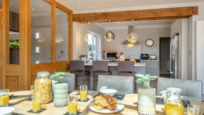 A breakfast setting with a wooden dining table, chairs, and a kitchen in the background. - 4 Bed in Hunstanton (oc-o44908) (Hunstanton)