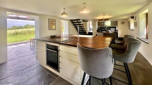 A spacious kitchen with a central island, bar stools, and a view of a green field. - 2 Bed in Milton Damerel (oc-s42659) (Milton Damerel)