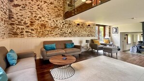 A modern living room with a stone wall, wooden floor, and a loft area with a staircase. - 2 Bed in Milton Damerel (oc-s42659) (Milton Damerel)