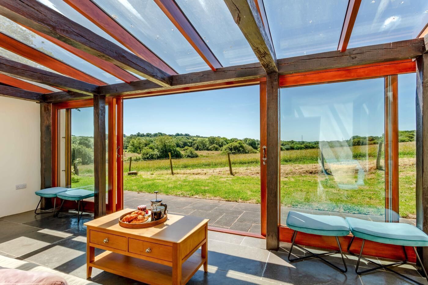 A room with a large glass door leading to an outdoor area, a wooden table with a tray of pastries, and two chairs.