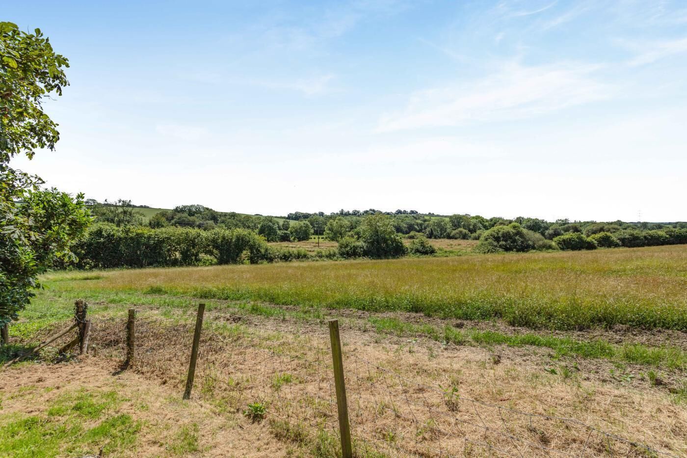 Een landelijk landschap met een veld, een hek en een boomrij in de verte.