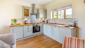 Une cuisine moderne avec des meubles gris, un plan de travail en bois, un four encastré, un four à micro-ondes et une fenêtre.