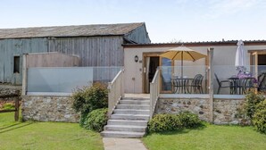 Un bâtiment rustique avec un escalier en pierre menant à un espace extérieur aménagé et abrité.