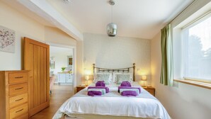 Une chambre à coucher comprenant un lit, des tables de chevet, une armoire, un luminaire suspendu et une fenêtre avec des rideaux.