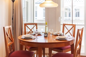 Une table de salle à manger ronde en bois, avec des chaises, une bouteille de vin et des verres disposés pour le repas.