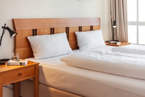 A neatly made bed with white linens, a wooden headboard, a bedside table with a lamp, and a nightstand with a book and glass. - Ferienwohnung Urlaub mit Hund (Sellin)
