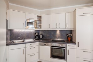 A modern kitchen with white cabinets, stainless steel appliances, a dishwasher, and a coffee maker. - Ferienwohnung Urlaub mit Hund (Sellin)