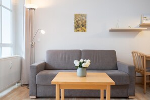 Un salon avec un canapé gris, une table en bois ornée d’un vase de fleurs, un lampadaire et un tableau accroché au mur.