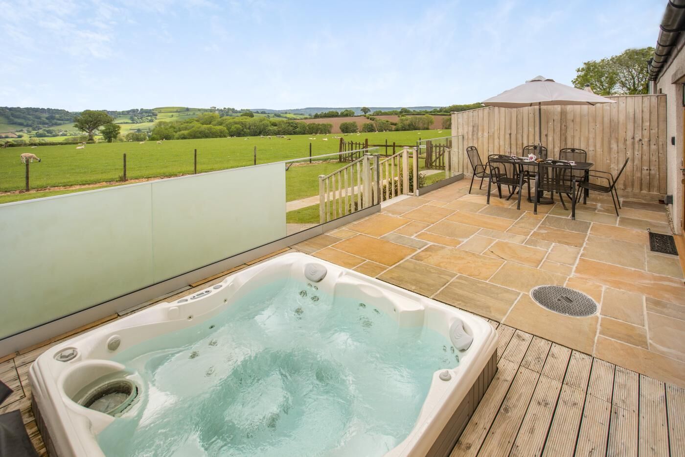 A hot tub on a wooden deck with a view of a green field and hills.