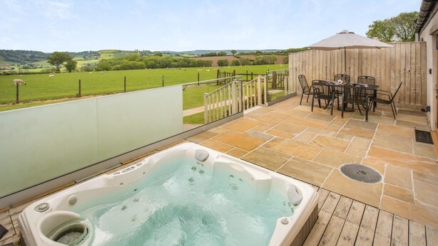 Een hottub op een houten terras met uitzicht op een groen veld en heuvels.