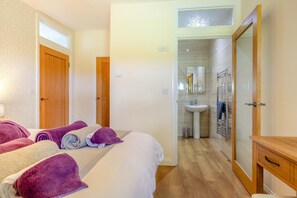 Ein Hotelzimmer mit einem Bett, Handtüchern, einem Nachttisch aus Holz und einem durch eine offene Tür einsehbaren Badezimmer.