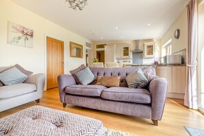 Ein Wohnzimmer mit Sofa, Hocker und einer Küche im Hintergrund.