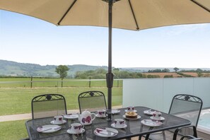 Eine Terrassengruppe im Freien mit einem für Tee gedeckten Tisch, umgeben von Stühlen und einem Sonnenschirm, der Schatten spendet.