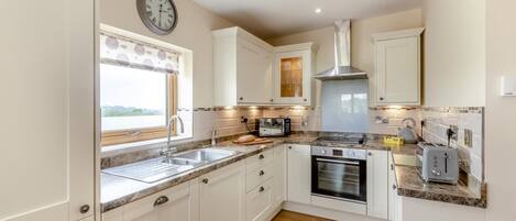 A modern kitchen with white cabinets, a built-in oven, a microwave, and a sink.