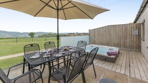An outdoor patio with a table set for tea, a hot tub, and a large umbrella. - 3 Bed in Dalwood (oc-c42675) (Dalwood)