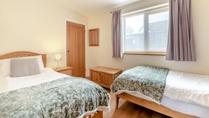 A bedroom with two beds, a wooden wardrobe, a bedside table with a lamp, and a window with curtains. - 3 Bed in Dalwood (oc-c42675) (Dalwood)