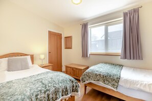 Ein Schlafzimmer mit zwei Betten, einem Holzschrank, einem Nachttisch mit Lampe und einem Fenster mit Vorhängen.