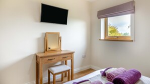 A bedroom with a bed, a wooden dresser, a mirror, a television, and a window with a view of trees. - 3 Bed in Dalwood (oc-c42675) (Dalwood)