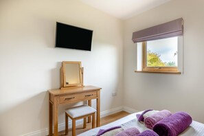 Ein Schlafzimmer mit einem Bett, einer Holzkommode, einem Spiegel, einem Fernseher und einem Fenster mit Blick auf Bäume.