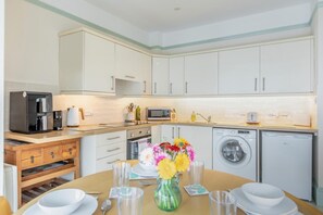 A modern kitchen with white cabinets, a coffee machine, a microwave, a washing machine, and a dining table set with plates and glasses. - 2 Bed in Beer (oc-g44900) (Beer)