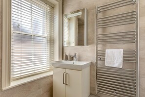 Ein Badezimmer mit Waschbecken, Spiegel, Handtuchhalter und einem Fenster mit Jalousien.