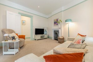 Ein Wohnzimmer mit Sofa, Sessel, Fernseher, Kamin und Lampe.