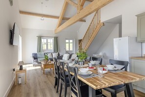 Une cuisine moderne avec un escalier en bois, un coin repas avec une table et des chaises en bois, et un salon avec un canapé et un téléviseur.