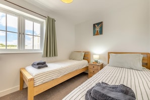 A bedroom with two single beds, a window with curtains, a bedside table with a lamp, and a painting on the wall. - 3 Bed in Meidrim (oc-c45350) (Meidrim)