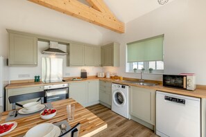 Une cuisine compacte dotée d’un plan de travail en bois, d’un lave-linge, d’un four à micro-ondes et d’un coin repas avec une table dressée pour deux personnes.