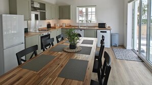 A modern kitchen with wooden beams, a dining area with a table and chairs, and a view through large windows. - 3 Bed in Meidrim (oc-c45350) (Meidrim)